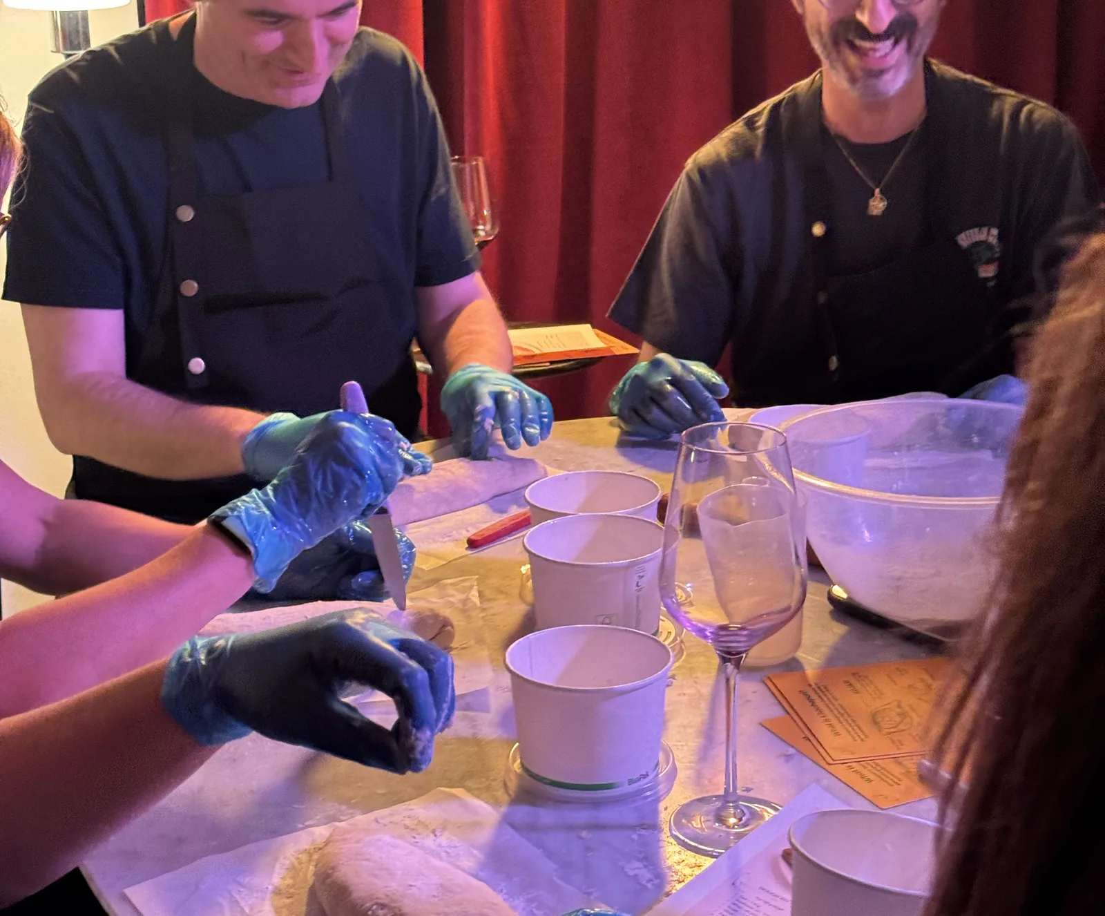 Guests working the dough at the marble table, wine glasses and take-home tubs beside them