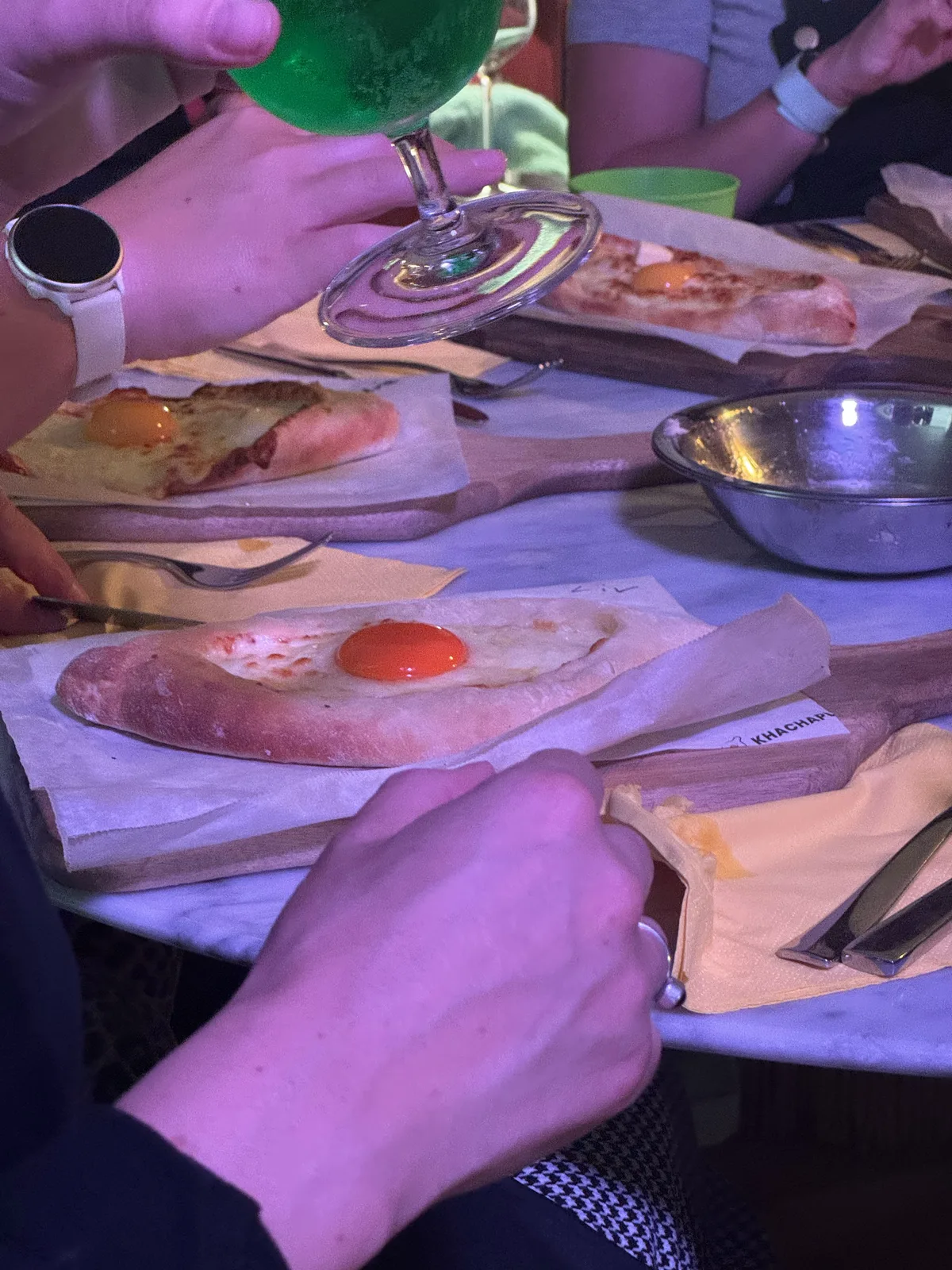 A finished adjaruli khachapuri with its egg yolk, wine being poured alongside